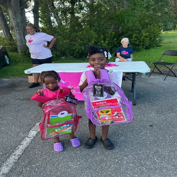 Two children smiling with backpacks at outdoor event