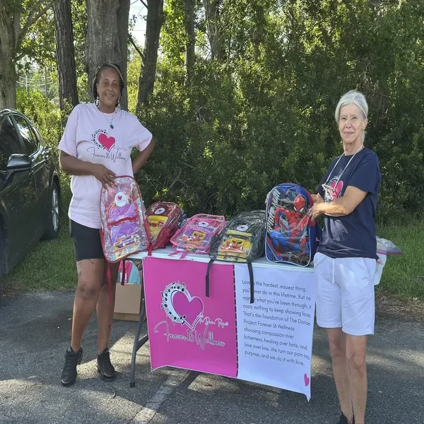 Two volunteers standing at Forever 16 Wellness table with backpacks