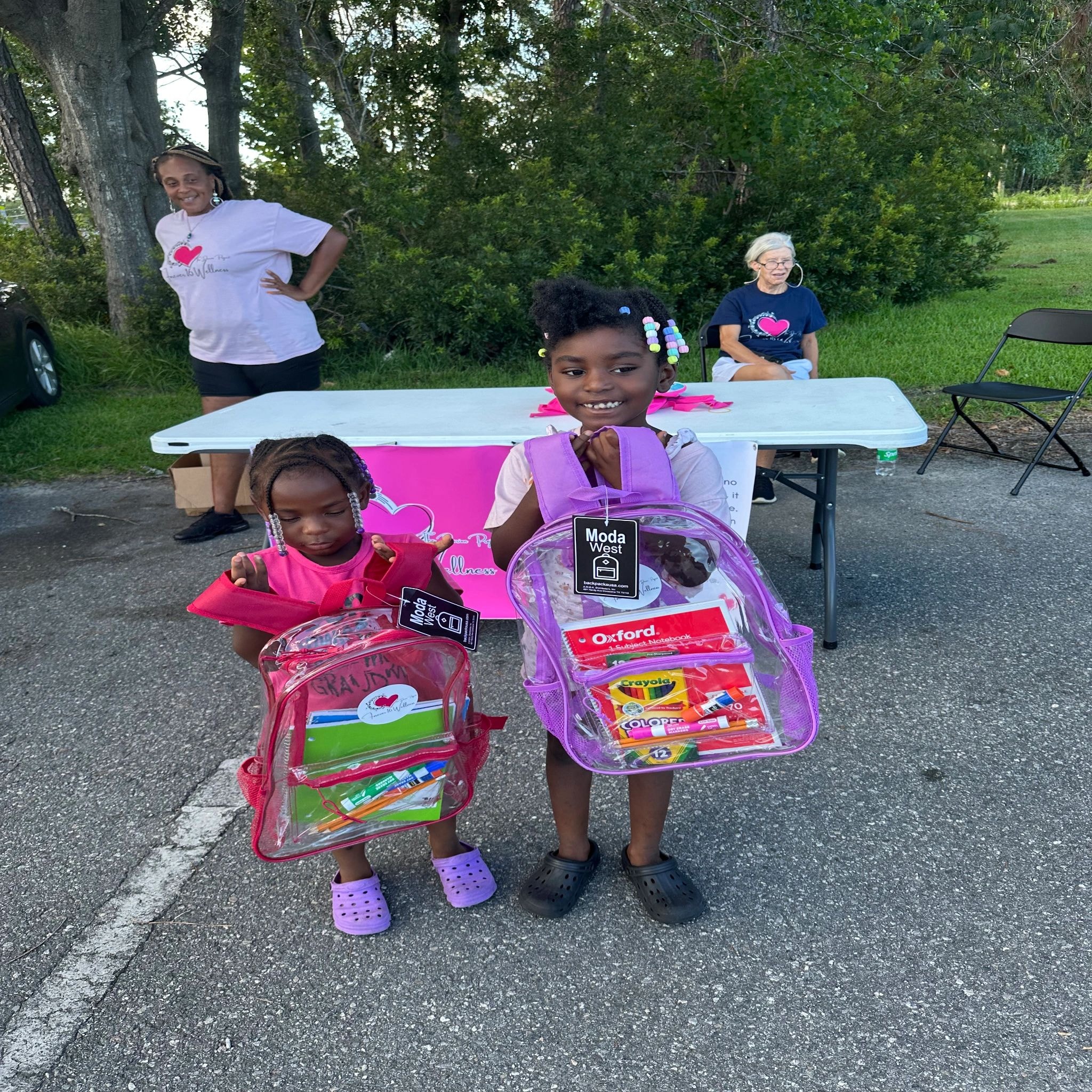 Three children holding backpacks at community giveaway